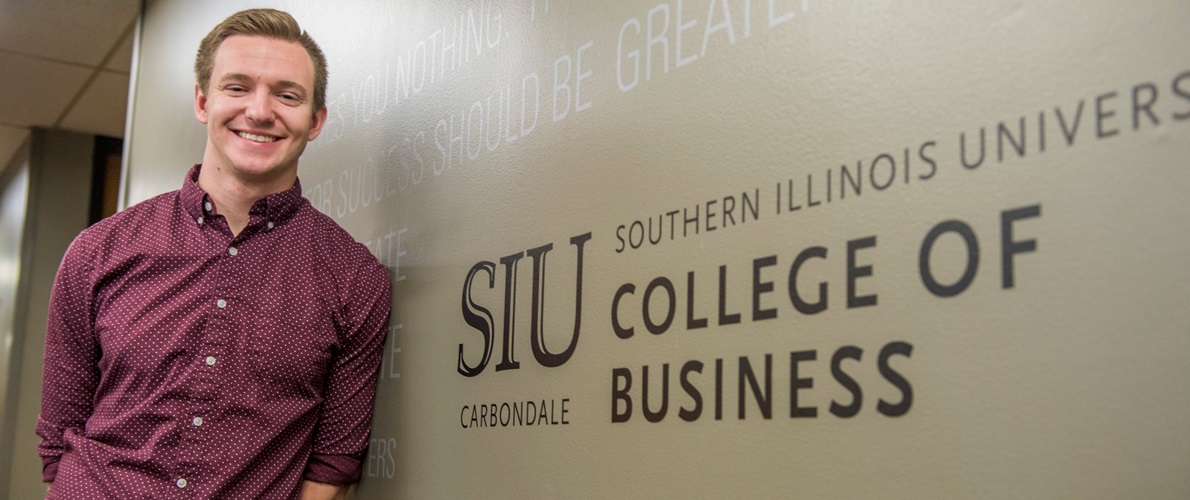 SIU Student standing in front of the College of Business and Analytics Wall