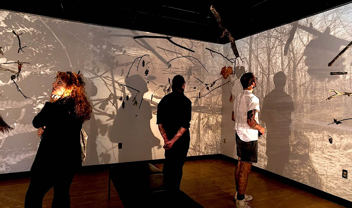 Three people view stills from SIU MFA graduate Leah Sutton's exhibit