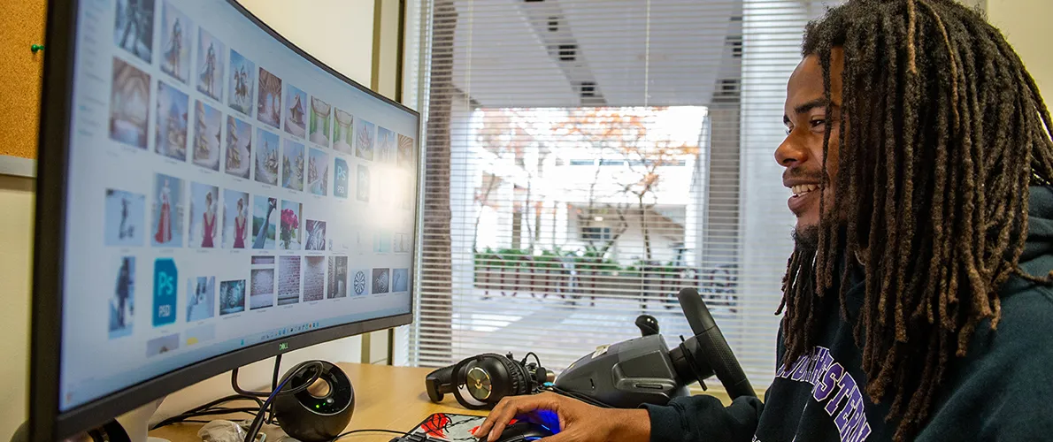 Student with long dreadlocks using a desktop computer to browse images on a large monitor