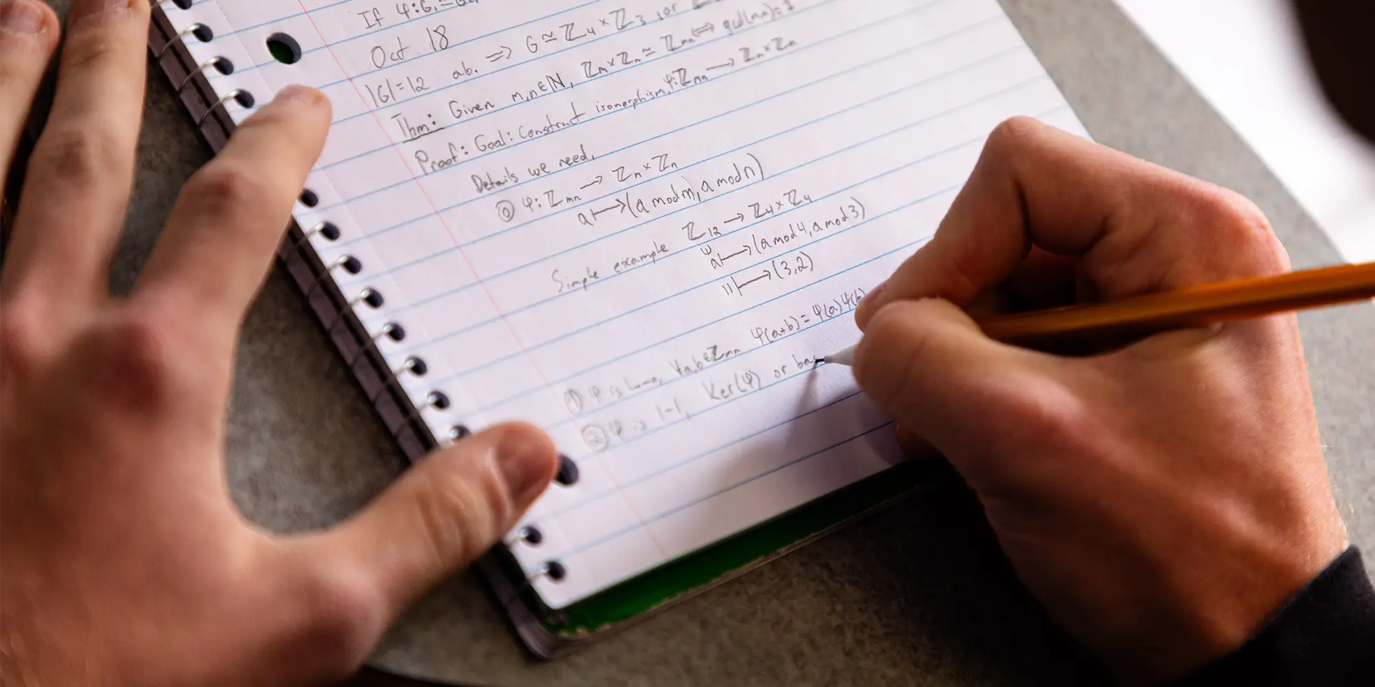 A student writes mathematical proofs and notation in a spiral notebook.