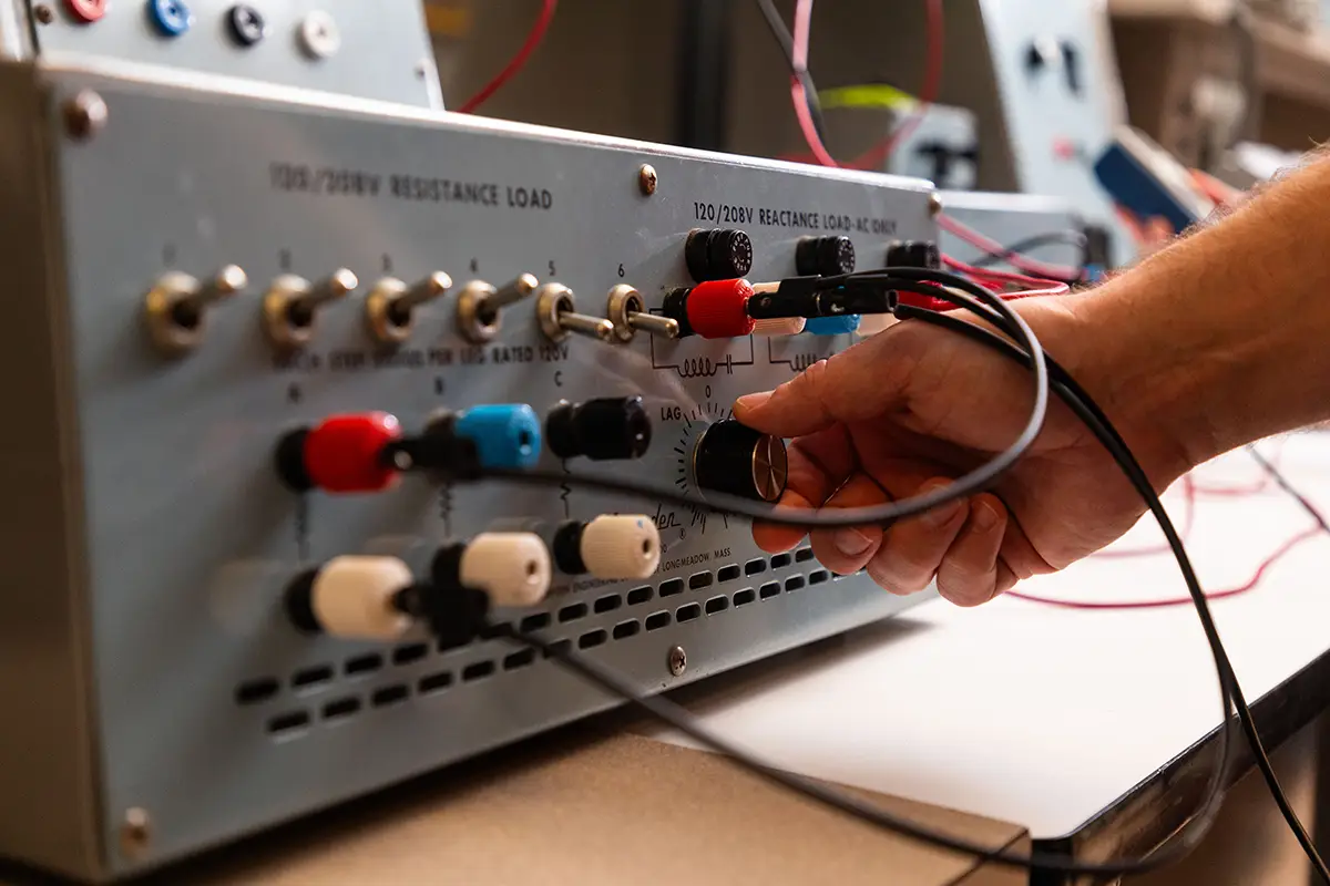 A student connects test leads to a resistance and reactance load training unit in an electrical engineering laboratory.