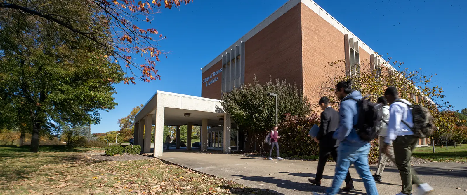 SIU students walking on sidewalk in front of Rehn Hall in fall.