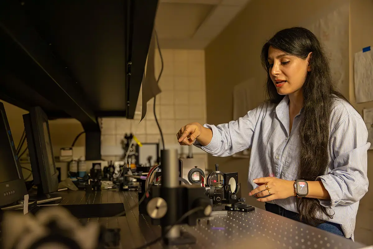 A researcher adjusts optical components on a laser optics bench in a darkened research laboratory.